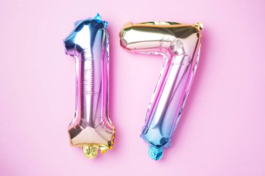 Yaratıcı düzen. Gökkuşağı folyo balon numarası, rakam 17. Doğum günü tebrik kartında 17 yazılıydı. Yıldönümü konsepti. Üst Manzara. Pembe arka planda şık renkli numara. Sayısal rakam.