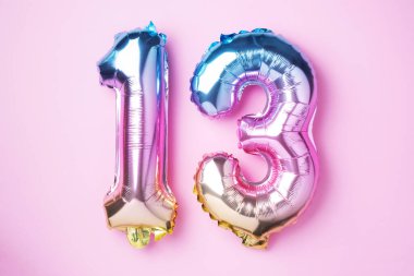 Yaratıcı düzen. Gökkuşağı folyo balon numarası, sayı 13. Üzerinde 13 yazan doğum günü tebrik kartı. Yıldönümü konsepti. Üst Manzara. Pembe arka planda şık renkli numara. Sayısal rakam.