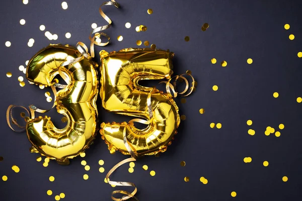 Altın folyo balon numarası, 35 haneli rakam. Doğum günü tebrik kartında 35 yazılıydı. Yıldönümü kutlaması. Pankart. Altın rakamlı, siyah arkaplan. Sayısal rakam, ışık bokeh, parıltı.
