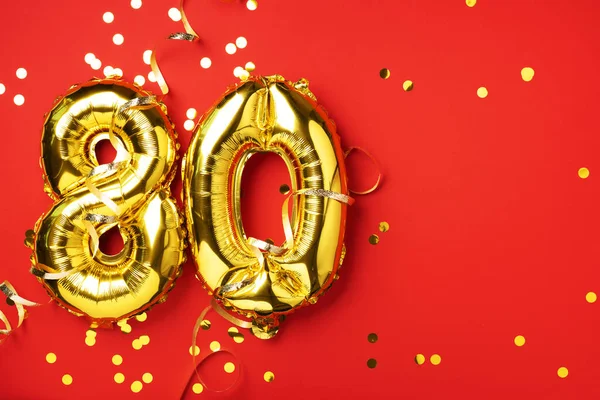 Altın folyo balon numarası, 80 haneli. 80 yazılı doğum günü tebrik kartı var. Yıldönümü kutlaması. Pankart. Altın rakamlı, kırmızı arkaplan. Sayısal rakam, parlak parlak parıltı