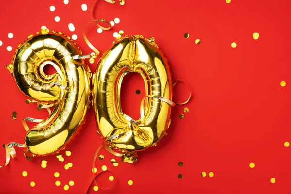 Altın folyo balon numarası, doksan haneli. Doğum günü tebrik kartı ve 90 numaralı yazı. Yıldönümü kutlaması. Pankart. Altın rakamlı, kırmızı arkaplan. Sayısal rakam, parlak parlak parıltı