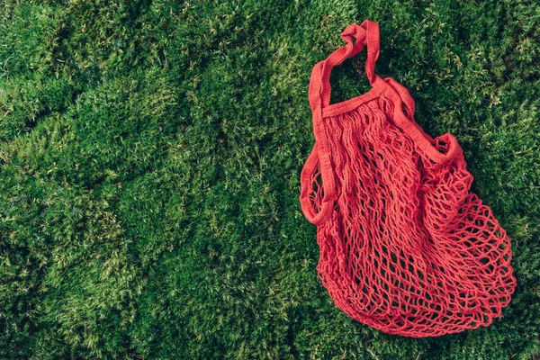 Reusable net bag or mesh shopper on green grass, moss background. Zero waste, plastic free concept. Top view. Eco friendly mesh shopper. Sustainable, ecology, organic lifestyle.