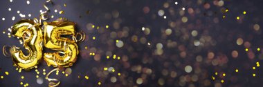 Altın folyo balon numarası, 35 haneli rakam. Doğum günü tebrik kartında 35 yazılıydı. Yıldönümü kutlaması. Pankart. Altın rakamlı, siyah arkaplan. Sayısal rakam, ışık bokeh, parıltı.