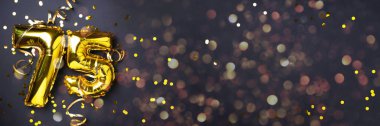 Altın folyo balon numarası, rakam 75. Doğum günü tebrik kartında 75 yazılıydı. Yıldönümü kutlaması. Pankart. Altın rakamlı, siyah arkaplan. Sayısal rakam, ışık bokeh, parıltı.