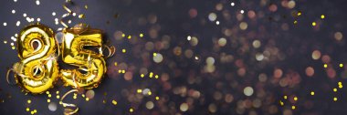 Altın folyo balon numarası, seksen beş. 85 yazısıyla birlikte doğum günü tebrik kartı. Yıldönümü kutlaması. Pankart. Altın rakamlı, siyah arkaplan. Sayısal rakam, ışık bokeh, parıltı.