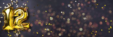 Altın folyo balon numarası, on iki numara. Doğum günü tebrik kartı, 12. yazı. Yıldönümü kutlaması. Pankart. Şık altın rakamlı, açık renkli, parlak, siyah arkaplan. Sayısal rakam.