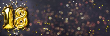 Altın folyo balon numarası, sayı 18. Doğum günü tebrik kartı, 18. yazı. Yıldönümü kutlaması. Pankart. Şık altın rakamlı, açık renkli, parlak, siyah arkaplan. Sayısal rakam.