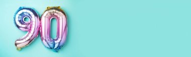 Gökkuşağı folyo balon numarası, doksan numara. Doğum günü tebrik kartı ve 90 numaralı yazı. Yıldönümü konsepti. Üst Manzara. Mavi arka planda renkli sayı. Sayısal rakam, kutlama olayı, şablon.