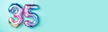 Gökkuşağı folyo balon numarası, rakam 35. Doğum günü tebrik kartında 35 yazılıydı. Yıldönümü konsepti. Üst Manzara. Mavi arka planda renkli sayı. Sayısal rakam, kutlama etkinliği.