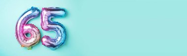 Gökkuşağı folyo balon numarası, rakam 65. Altmış beş yazılı doğum günü tebrik kartı. Yıldönümü konsepti. Üst Manzara. Mavi arka planda renkli sayı. Sayısal rakam, kutlama etkinliği.