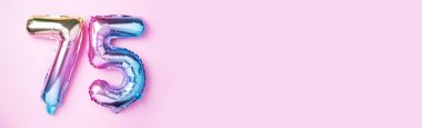 Gökkuşağı folyo balon numarası, rakam 75. Doğum günü tebrik kartında 75 yazılıydı. Yıldönümü konsepti. Üst Manzara. Pembe arka planda renkli sayı. Sayısal rakam, kutlama etkinliği.