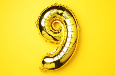 Yaratıcı düzen. Altın folyo balon numarası ve 99. rakam. Doğum günü tebrik kartı. Yıldönümü konsepti. Üst Manzara. Uzayı kopyala Sarı arkaplan üzerinde zarif altın rakam. Sayısal rakam