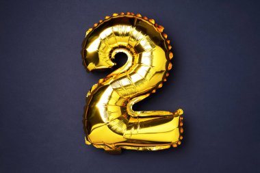 Creative layout. Golden foil balloon number and digit two 2. Birthday greeting card. Anniversary concept. Top view. Copy space. Stylish gold numeral over black background. Numerical digit