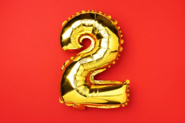 Yaratıcı düzen. Altın folyo balon numarası ve 2 haneli rakam. Doğum günü tebrik kartı. Yıldönümü konsepti. Üst Manzara. Uzayı kopyala Kırmızı zemin üzerinde zarif altın rakam. Sayısal rakam