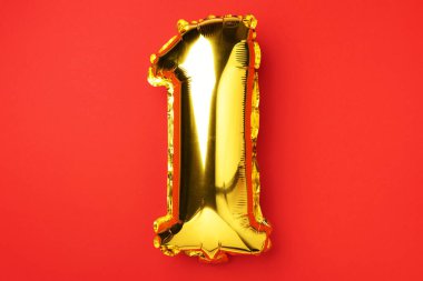 Yaratıcı düzen. Altın folyo balon numarası ve sayı 1 1. Doğum günü tebrik kartı. Yıldönümü konsepti. Üst Manzara. Uzayı kopyala Kırmızı zemin üzerinde zarif altın rakam. Sayısal rakam.