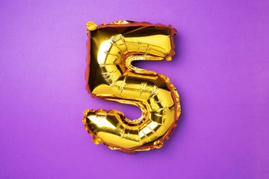Creative layout. Golden foil balloon number and digit five 5. Birthday greeting card. Anniversary concept. Top view. Copy space. Stylish gold numeral over purple background. Numerical digit