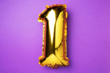 Creative layout. Golden foil balloon number and digit one 1. Birthday greeting card. Anniversary concept. Top view. Copy space. Stylish gold numeral over purple background. Numerical digit.