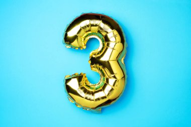 Yaratıcı düzen. Altın folyo balon numarası ve 3 haneli rakam. Doğum günü tebrik kartı. Yıldönümü konsepti. Üst Manzara. Uzayı kopyala Mavi arka planda zarif altın rakamı. Sayısal rakam