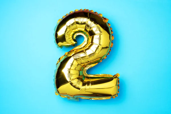 Creative layout. Golden foil balloon number and digit two 2. Birthday greeting card. Anniversary concept. Top view. Copy space. Stylish gold numeral over blue background. Numerical digit