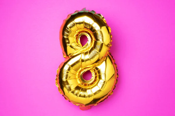 8 March. Happy Women\'s Day. Creative layout. Golden foil balloon number, digit eight 8. Birthday greeting card. Anniversary concept. Top view. Gold numeral over pink background. Numerical digit.