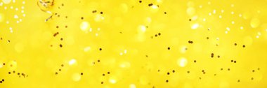 New year, Christmas background. Golden shiny glitter, sparkles, light bokeh on yellow background. Banner with copy space. Festive backdrop for greeting card.