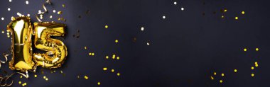 Altın folyo balon numarası, rakam 15. Doğum günü tebrik kartı, 15. yazı. Yıldönümü kutlaması. Pankart. Şık altın rakamlı, açık renkli, parlak, siyah arkaplan. Sayısal rakam.