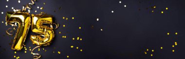 Altın folyo balon numarası, rakam 75. Doğum günü tebrik kartında 75 yazılıydı. Yıldönümü kutlaması. Pankart. Altın rakamlı, siyah arkaplan. Sayısal rakam, ışık bokeh, parıltı.