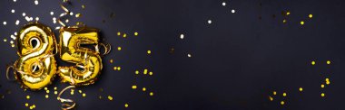 Altın folyo balon numarası, seksen beş. 85 yazısıyla birlikte doğum günü tebrik kartı. Yıldönümü kutlaması. Pankart. Altın rakamlı, siyah arkaplan. Sayısal rakam, ışık bokeh, parıltı.