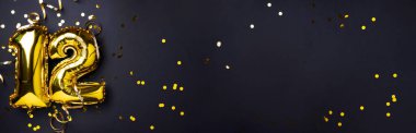 Altın folyo balon numarası, on iki numara. Doğum günü tebrik kartı, 12. yazı. Yıldönümü kutlaması. Pankart. Şık altın rakamlı, açık renkli, parlak, siyah arkaplan. Sayısal rakam.