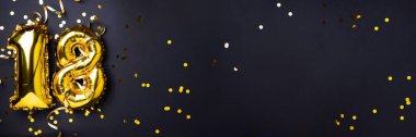 Altın folyo balon numarası, sayı 18. Doğum günü tebrik kartı, 18. yazı. Yıldönümü kutlaması. Pankart. Şık altın rakamlı, açık renkli, parlak, siyah arkaplan. Sayısal rakam.