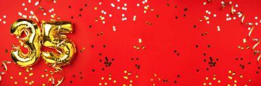 Altın folyo balon numarası, 35 haneli rakam. Doğum günü tebrik kartında 35 yazılıydı. Yıldönümü kutlaması. Pankart. Altın rakamlı, kırmızı arkaplan. Sayısal rakam, ışık bokeh, parıltı.