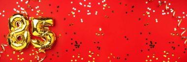 Altın folyo balon numarası, seksen beş. 85 yazısıyla birlikte doğum günü tebrik kartı. Yıldönümü kutlaması. Pankart. Altın rakamlı, kırmızı arkaplan. Sayısal rakam, ışık bokeh, parıltı.
