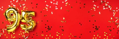 Altın folyo balon numarası, doksan beş. Doğum günü tebrik kartında 95 yazılıydı. Yıldönümü kutlaması. Pankart. Altın rakamlı, kırmızı arkaplan. Sayısal rakam, ışık bokeh, parıltı.