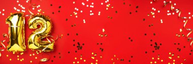 Altın folyo balon numarası, on iki numara. Doğum günü tebrik kartı, 12. yazı. Yıldönümü kutlaması. Pankart. Şık altın rakamlı, parlak, kırmızı arkaplan. Sayısal rakam.