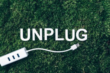 Word Unplug, white internet usb adapter on moss, green grass background. Top view. Copy space. Banner. Biophilia concept. Nature backdrop. clipart