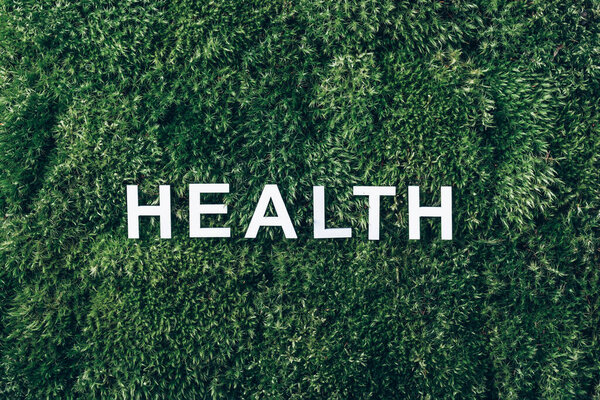 Word Health on moss, green grass background. Top view. Copy space. Banner. Biophilia trend. Nature backdrop. Mental Health concept.