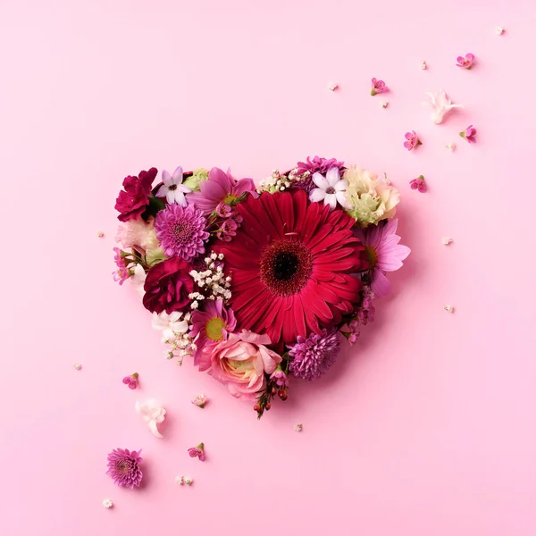 Forma de corazón hecha de flores de primavera sobre fondo rosa pastel perforado. Vista superior, cama plana. Concepto de verano. Día de San Valentín. Diseño creativo. —  Fotos de Stock