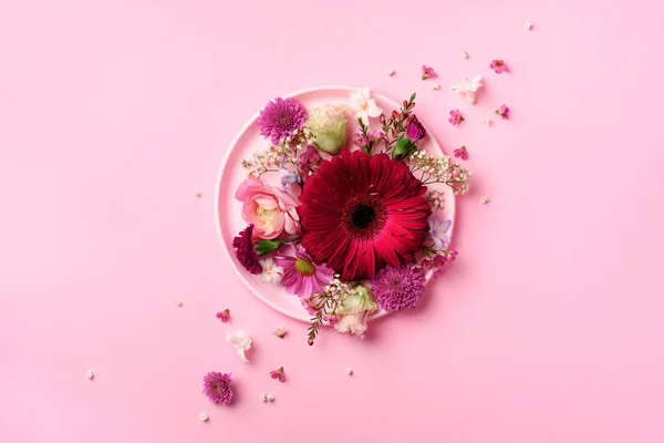 Gerberas y flores de primavera sobre plato rosado sobre fondo pastel. Vista superior, cama plana. Cultivo cuadrado con espacio de copia. Concepto de verano —  Fotos de Stock