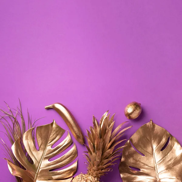 Frutas exóticas douradas, palma tropical, folhas monstera em fundo violeta. Vista superior. Deitado. Conceito de comida. Layout criativo de abacaxi dourado, banana, limão com espaço de cópia. — Fotografia de Stock