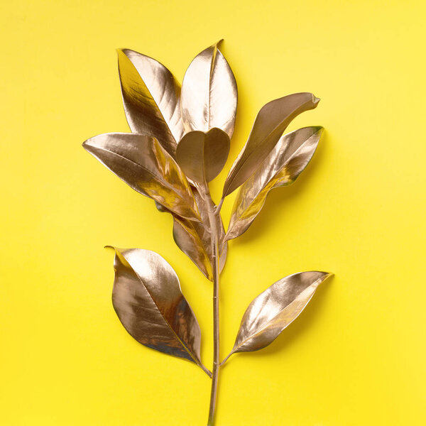 Floral minimal style concept. Exotic summer trend. Golden tropical leaves and branch on yellow color background. Shiny and sparkle design, fashion concept.