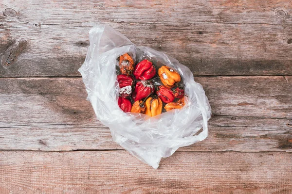 Moldy and wrinkled rotten peppers in plastic bag on wooden background. Concept of unhealthy, decompose, spoiled vegetables. Garbage dump rotten food. Top view. Copy space. Waste concept. Store packets