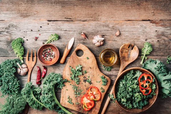 Fresh kale in bowl, wooden spoon, fork, chopping board, spices, salt, garlic, pepper on rustic wooden background. Top view. Copy space. Zero waste, organic vegetables concept. Vegan and vegetarian — Stock Photo, Image