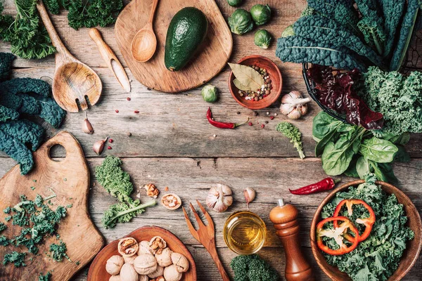 Orgnic hälsosam vegansk mat matlagning ingredienser. Högst upp. Uppfattat utrymme. Gröna grönsaker, frön, avokado, nötter, grönkål, kryddor, salt, träredskap på trä bakgrund. Ren mat, noll avfall — Stockfoto