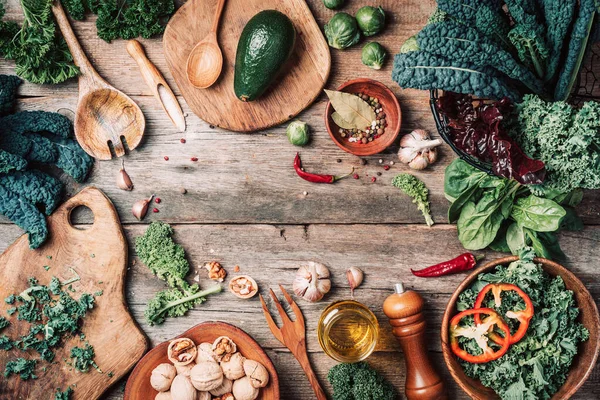 Orgnic healthy vegan food cooking ingredients. Top view. Copy space. Green vegetables, seeds, avocado, nuts, kale, spices, salt, wooden utensils on wood background. Clean eating food, zero waste — Stock Photo, Image