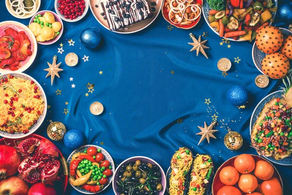 Веганская еда и блюда. Рождественский или новогодний праздничный семейный ужин, салаты, фрукты, овощи, блестки звезд на синем фоне. Здоровое, чистое питание. Веганская или безглютеновая диета Стоковая Картинка