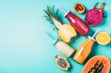 Detox yaz içeceği. Vejetaryen, vejetaryen, früktoryan diyeti. Taze smoothie ve sulu meyveler - papaya, portakal, ananas, ejderha meyvesi, pitahaya, tamarillo meyvesi mavi arka planda. Üst manzara, düz uzanma