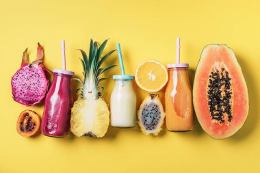 Detox yaz içeceği. Vejetaryen, vejetaryen, früktoryan diyeti. Taze smoothie ve sulu meyveler - papaya, portakal, ananas, ejderha meyvesi, pitahaya, tamarillo meyvesi sarı arka planda. Üst manzara, düz uzanma