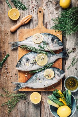 Çiğ dorado balığı, malzeme, limon, otlar, yağ, sebze ve baharatlar ahşap arka planda ahşap kesim tahtasında. Üst Manzara. Sağlıklı beslenme. Yemek deseni. Deniz ürünleri konsepti.