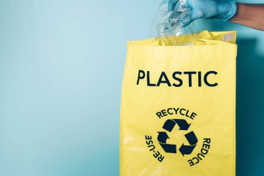 Mavi eldivenler geri dönüşüm kutusuna plastik şişe koyar. Çevre bakımı, atık ayıklama. Uzayı kopyala Koronavirüs pandemik karantinasından sonra yeni normal bir hayat. Geri dönüşüm, sıfır atık, ekoloji kavramı.