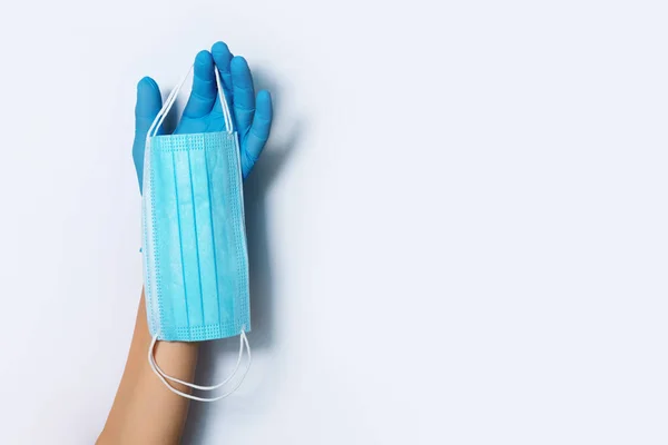 Hand met blauwe medische handschoenen met medisch gezichtsmasker op witte achtergrond. Banner met kopieerruimte. Apparatuur ter bescherming van de gezondheid tijdens een pandemie met het Coronavirus. Blijf veilig. Covidiënt 19 — Stockfoto